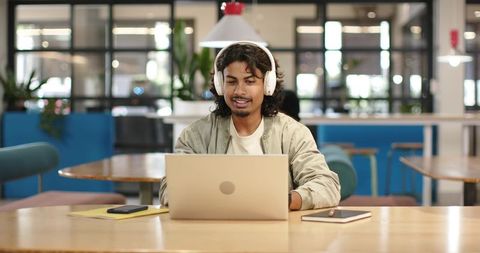 African american man working on laptop wearing white headphones in modern coworking hub