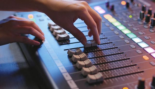 Hands adjusting mixing console faders with colorful led lights in recording studio