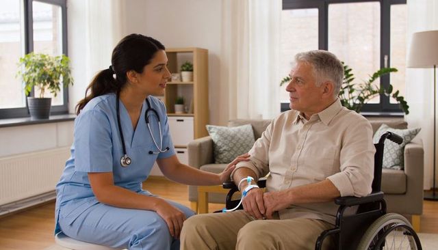 Nurse kneeling beside senior in wheelchair checking iv, compassionate home care visit