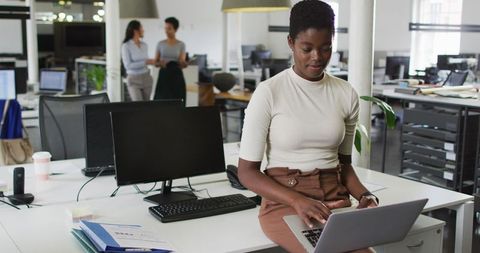 Confident Businesswoman Using Laptop at Workstation with Colleagues