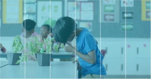 Leaning boy wiping face with tissue in classroom near potted plants