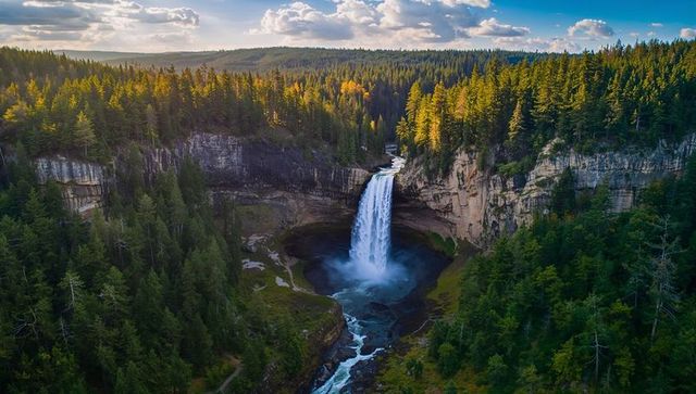 Plunging waterfall cascading into forested canyon with mist and winding river