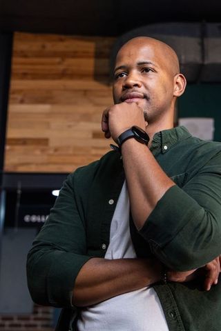 African man contemplating in coworking lounge wearing smartwatch and casual green shirt
