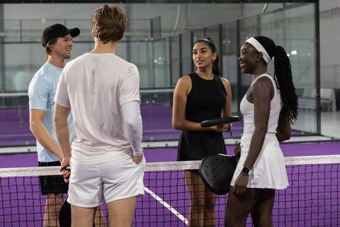 Diverse pickleball players chatting at net on vibrant purple indoor court holding paddles