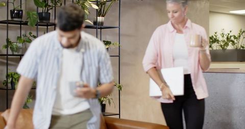 Diverse Coworkers in Office Lounge with Coffee and Laptop by Plant Shelf