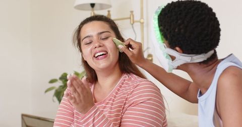 Friends sharing at-home skincare routine with led face mask and cucumber pads