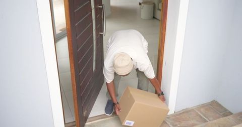 Delivery worker placing parcel at doorway wearing beige knit cap and casual shoes