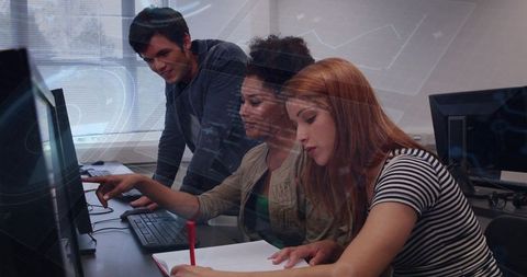 Diverse students collaborating at computer workstation, coding and note taking in classroom