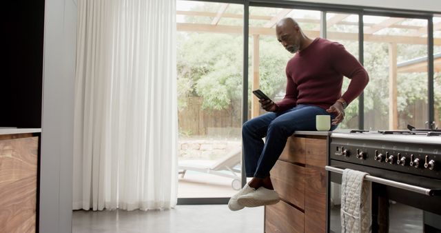 Senior Man Using Smartphone while Sitting on Kitchen Counter - Download Free Stock Images Pikwizard.com