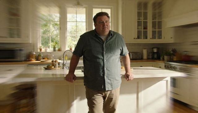 Leaning midlife man in casual green shirt at sunlit modern kitchen island