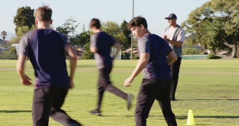 Coach guiding male athletes during cone drill running laps on field for speed conditioning