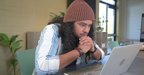 Leaning forward and studying laptop in modern workspace wearing beanie and bracelets