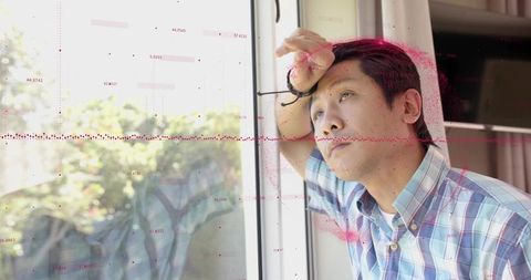 Contemplative man leaning on window, gripping glasses and gazing outward with data overlay