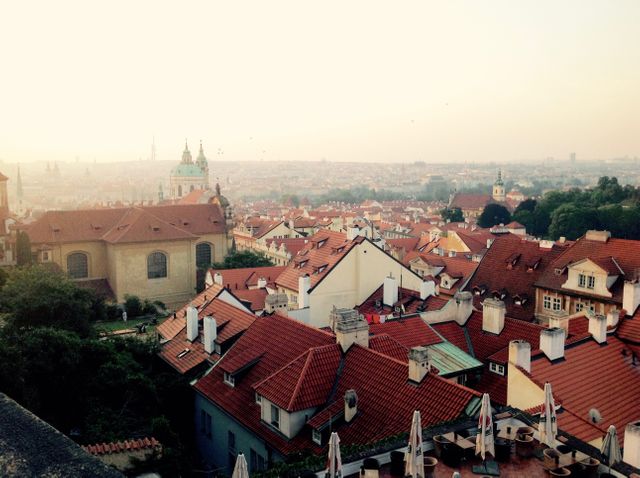 This image showcases an aerial view of Prague's iconic red rooftops, set against a picturesque sunset. It highlights the historic architecture of the city, capturing the charming scenery and urban layout. Perfect for use in travel blogs, brochures, tourism advertisements, and any content related to European travel, cityscapes, and cultural heritage.