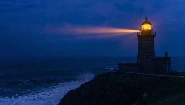 Lighthouse beacon guiding stormy coastline at dusk, warm rotating beam over surf