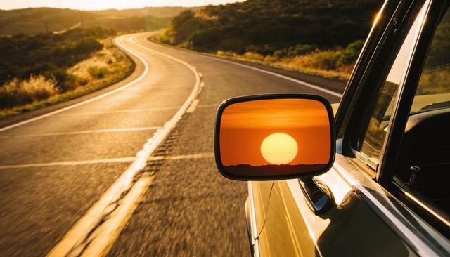Sunset reflection in car mirror on winding country road at golden hour