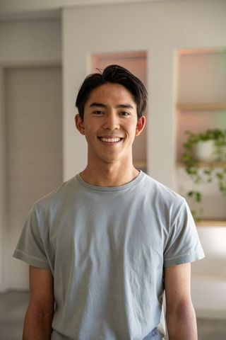 Smiling asian man standing in modern home wearing light gray t-shirt, casual lifestyle