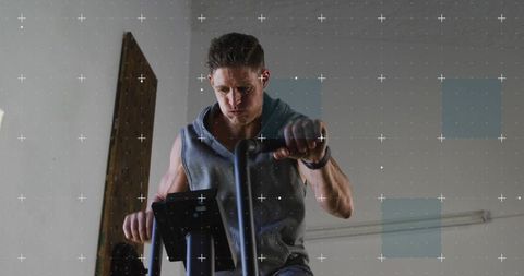 Male athlete pedaling on stationary bike wearing gray sleeveless hoodie and smartwatch