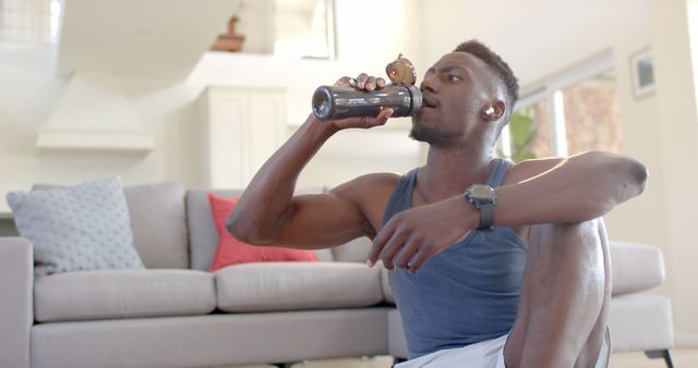 Young man in activewear resting with a drink after home workout - Download Free Stock Images Pikwizard.com