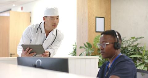 Healthcare team collaborating at clinic reception using tablet and computer with headset