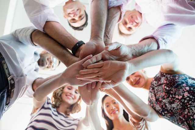 Diverse group of business colleagues stacking hands in a show of unity and teamwork. Ideal for illustrating concepts of collaboration, team spirit, corporate culture, and successful partnerships. Suitable for use in business presentations, team-building materials, and corporate websites.