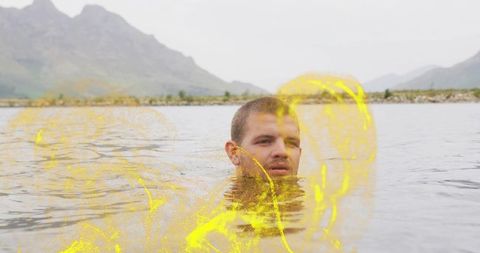 Man emerging from mountain lake with vibrant yellow pigment swirls and serene landscape