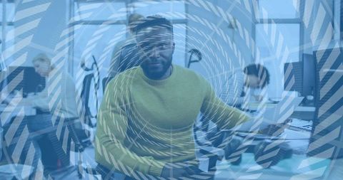 Mid-career man in green sweater typing at keyboard in modern open-plan office with spiral overlay