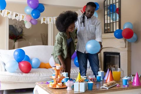 Couple decorating living room for birthday party with balloons, cupcakes, gifts and snacks