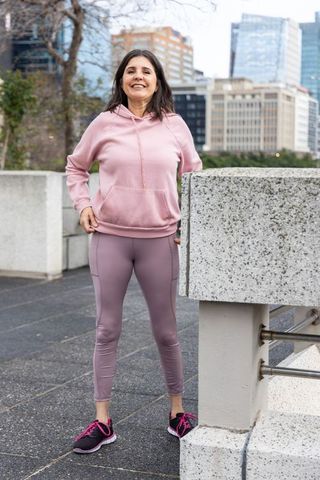 Smiling middle-aged woman standing on urban terrace wearing pink hoodie and mauve leggings