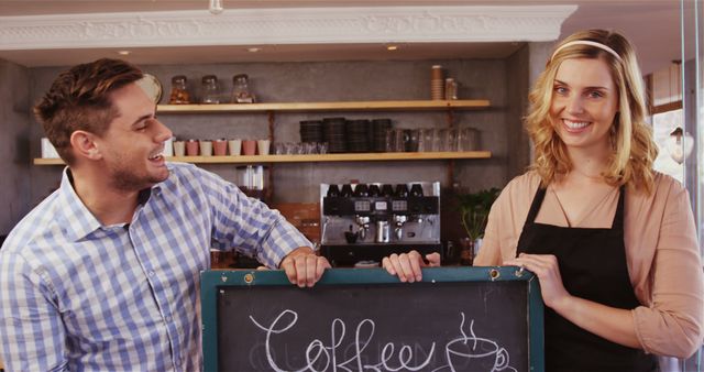 Young man and woman baristas standing behind counter display chalkboard coffee sign. Use for small business promotions, cafe advertising, hospitality training materials.