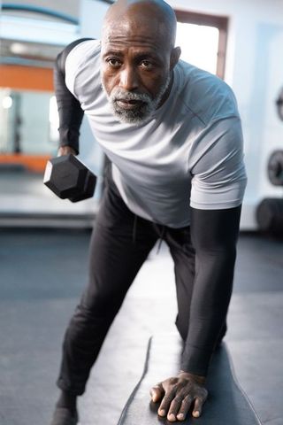 Senior african american man lifting dumbbell during focused strength training in gym