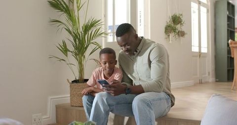 African american father and son sharing smartphone on home step, everyday bonding