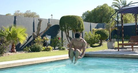 African american man jumping cannonball into backyard pool on sunny summer day splash action