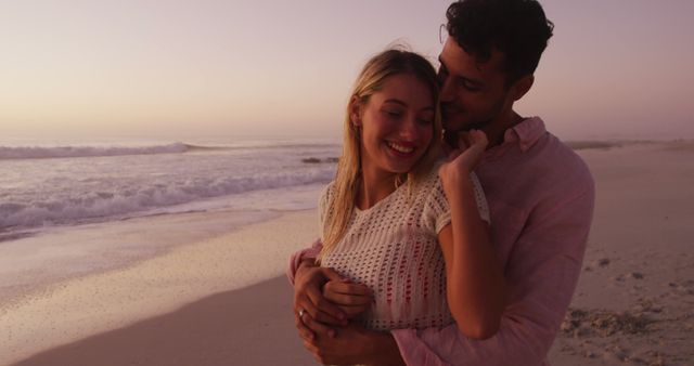 Couple embracing on a sandy beach during sunset, wearing casual attire. Ideal for themes of romance, coastal vacations, relationships, and serene, happy moments spent together. Perfect for travel brochures, romantic greeting cards, lifestyle blogs, and social media posts celebrating love and togetherness.