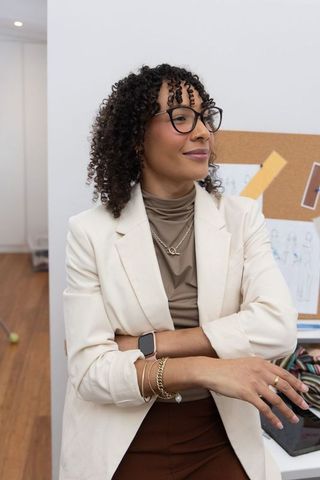 African american fashion designer standing arms crossed wearing cream blazer and glasses