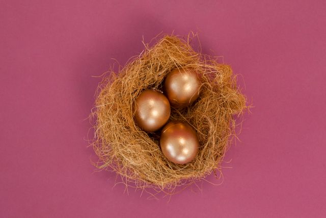Golden Easter eggs resting in a nest on a pink background. Ideal for Easter-themed promotions, holiday decorations, and festive greeting cards. The vibrant colors and shiny metallic eggs add a touch of luxury and celebration to any project.
