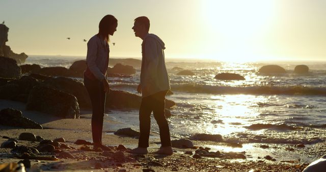 A young Caucasian couple enjoys a romantic moment on the beach at sunset, with copy space. Their silhouettes against the golden light create a serene and intimate atmosphere.