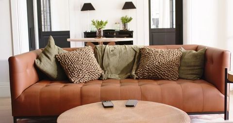 Caramel leather tufted sofa with olive throw and chunky pillows in cozy modern living room