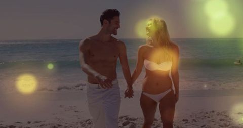 Romantic sunlit couple walking hand in hand on beach at golden hour with bokeh lens flare