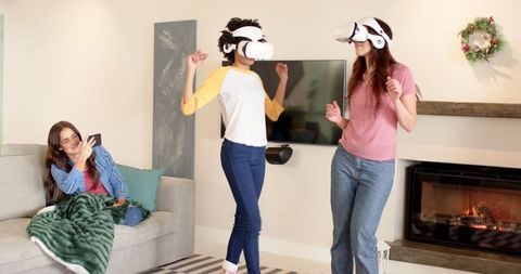 Two friends enjoying virtual reality experiences in a comfortable living room, showcasing technological excitement and innovation. Ideal for promoting VR technology, home entertainment systems, or leisure and lifestyle content. Perfect for illustrating modern lifestyle, tech engagement, and social connections indoors.