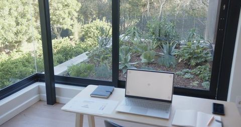 Minimalist home office with laptop near corner glass windows and lush succulent planter