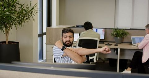 Businessman stretching while colleagues work on laptops