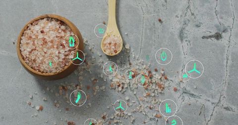 Himalayan pink salt in wooden bowl with spoon and teal wellness icons on concrete slab