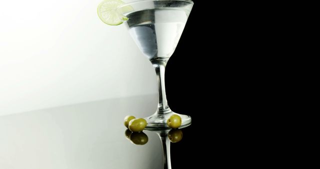 A martini glass with a clear beverage is garnished with a lime wedge and accompanied by two olives, with copy space. Its elegant presentation suggests a sophisticated atmosphere for socializing or celebrating.