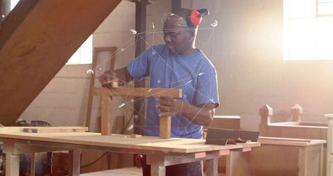 Mature woodworker wearing ear protection assembling wooden frame at sunlit workshop bench
