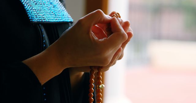 Biracial woman holding beads and praying at home, copy space. Religion, spirituality and house, unaltered.