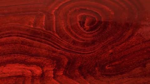 Camera panning and focusing on recentering knot in deep-red varnished wood grain closeup