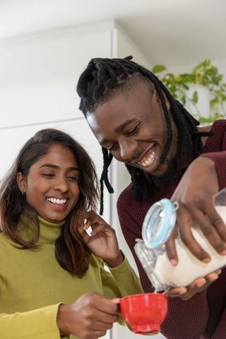 Smiling african american man and indian woman pouring powder from glass jar into red cup
