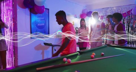 Young adults playing pool at neon birthday party with disco lights and balloons