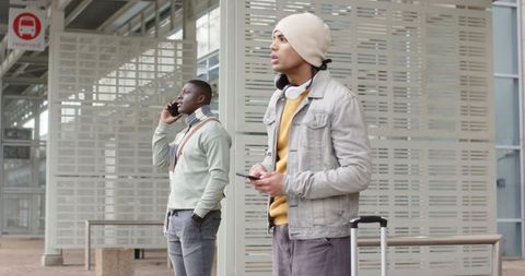 Multiethnic commuters waiting at urban transit stop with suitcase headphones smartphones